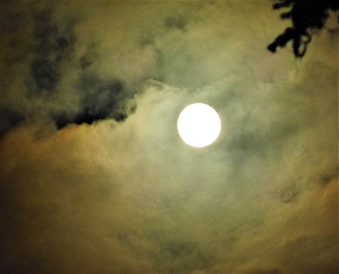 a light of full moon peaks through the clouds